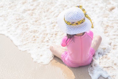 the little cute girl wearing pink swimwear with white beach hat and sitting, playing on the beach