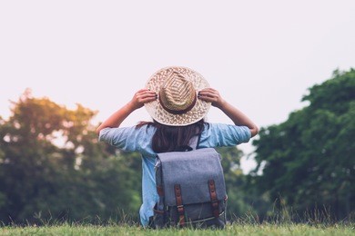 woman traveler with backpack holding hat and looking at the view in forest, travel concept