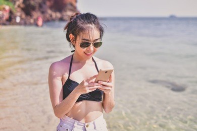 swimsuit concept. beautiful girl wearing a swimsuit playing mobile on the beach. beautiful girl is traveling on the beach. beautiful girls are happy.