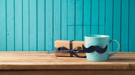 happy fathers day concept with coffee cup, mustache and gift box over wooden background