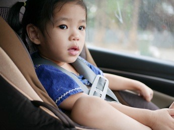 selective focus and close up of asian baby girl sitting on a car seat with belt fasten in a moving / driving car - for baby safety, always have the belt fasten when putting young little baby in a car