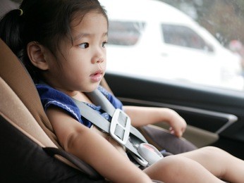 selective focus and close up of asian baby girl sitting on a car seat with belt fasten in a moving / driving car - for baby safety, always have the belt fasten when putting young little baby in a car