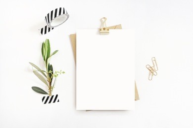 feminine stationery,  desktop mock-up scene. blank greeting card, craft envelope, washi tape and golden paper, binder clips with olive branch.white table background. flat lay, top view. 