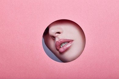woman looking in the hole, bright beautiful makeup, big eyes and lips, bright lipstick, professional cosmetics and facial care. bright colored background and a gap slot in the paper