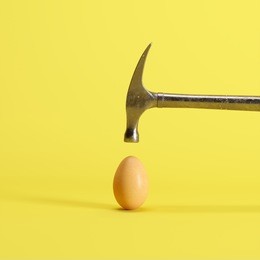 hammer is hitting on an egg with yellow background. minimal idea creative concept.