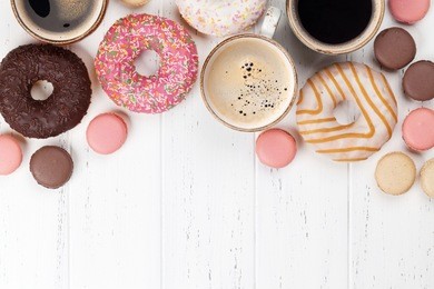 coffee cups, donuts and macaroons on white wooden table. top view with space for your text