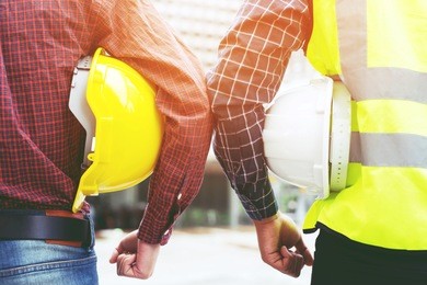 close up back view of engineering male two construction worker holding safety yellow helmet and white helmet with wear reflective clothing for the safety of the work operation. outdoor of building.