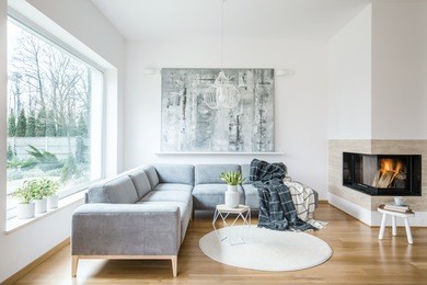 white sitting room interior with grey corner sofa, tulips in vase placed on an end table, fireplace and modern art painting