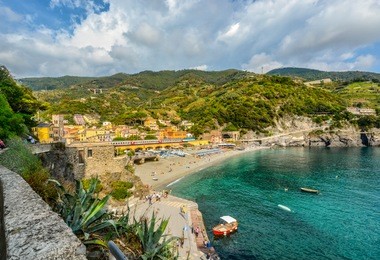 the sandy beach spiaggia di fegina, the railway with trains running, the mountains, sea and colorful village of monterosso al mare, cinque terre italy