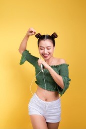fashion smiling asian woman listening to music in earphones  over yellow background