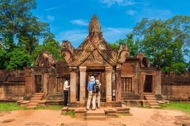 tourists admiring the east gopura of the second enclosure with the amazing carved pediment made of red sandstone in the banteay srei (citadel of the women) temple in cambodia.