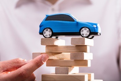 blue car over businessperson's finger arranging wooden blocks. 