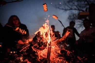 young and cheerful friends sitting and fry marshmallows of the foreground of bonfire in the deep night on the nature