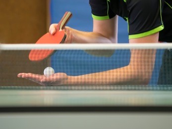 table tennis player serving, focus at the ball in the background behind the net