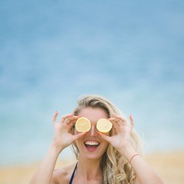 young attractive woman covering her eyes with lemon slices. cheerful girl on the beach