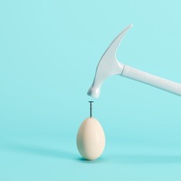 white hammer is driving a nail into a white egg with blue background. minimal idea creative concept.