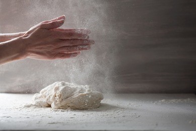 woman making home made french bread dough. sprinkling flour onto the dough, which is on a white marble countertop. horizontal.