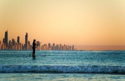 single paddler against the gold coast skyline at sunset.