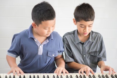 asian student boys playing piano together in the class