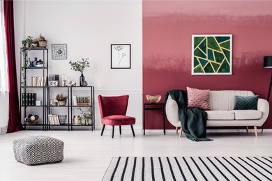 striped carpet and pouf in spacious living room interior with red armchair and green painting