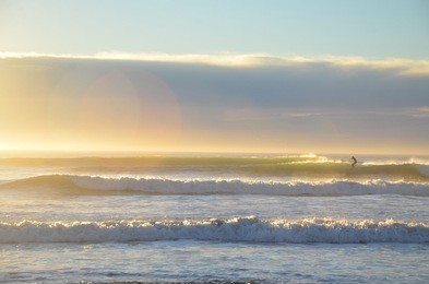 a surfer surfing at the new brighton beach. it's a best spot to visit for sunrise and play amongst the waves under the pier or maybe take a stroll along the top and watch the fishermen.