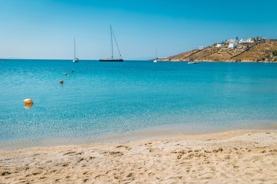 mykonos island, famous ornos beach organized with sun beds emerald clear water beach of ornos in island of mykonos, cyclades, greece