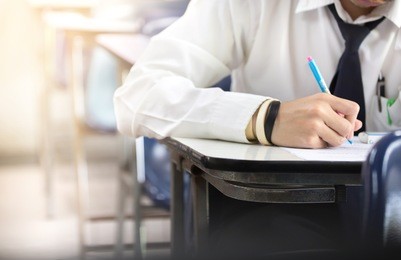soft focus.hand high school or university student in uniform holding pencil writing on paper answer sheet.sitting on lecture chair taking final exam attending in examination room or classroom.