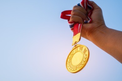 winners champion in success award concept : woman hands raised holding gold medals with ribbon against blue sky background to show success in sport or business