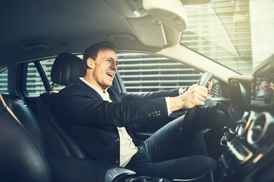 smiling young businessman wearing a blazer singing while driving his car through the city during his morning commute to work