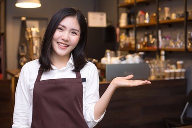 asian women barista smiling and looking to camera in coffee shop counter.  barista female working at cafe. working woman small business owner or sme concept.