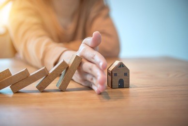 woman hand stopping risk the wooden blocks from falling on house, home insurance and security concept.
