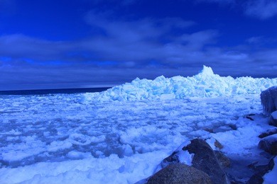 bright blue ice wall on the shores of nottawasaga bay in meaford, ontario. these images show the wall in both close-ups and from further away. the ice has a blue tint and the sky and water are vivid. 