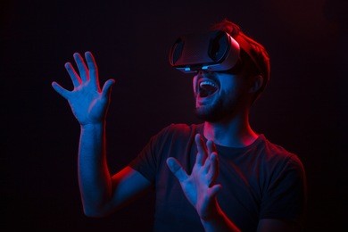 casual man using glasses of virtual reality and exploring another world with great excitement in neon dark lights. 