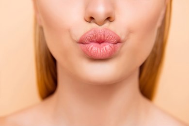 air kiss for you. close up cropped shot of femenine gorgeous charming adorable lady with nude natural full big pout lips isolated on beige background, perfection wellness wellbeing concept