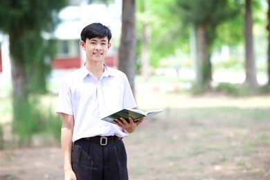thai boy in thai student uniform (black shorts) with nature background, also holding book in his hand
