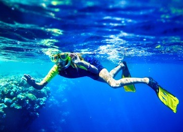 child scuba diver with group coral fish in  blue water.
