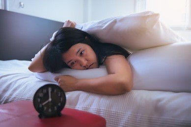 young asian woman hates getting stressed waking up early,female stretching her hand to ringing alarm to turn off alarm clock