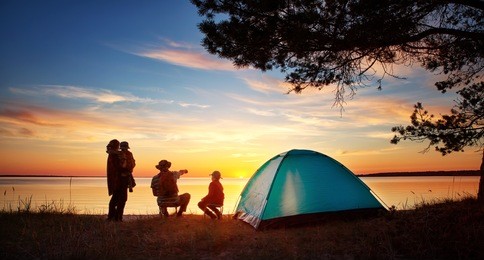 family resting with tent in nature at sunset. woman, man and children near seaside
