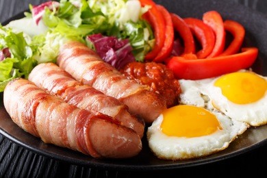 homemade fried sausages wrapped in bacon, eggs, sauce and fresh salad close-up on a plate. horizontal