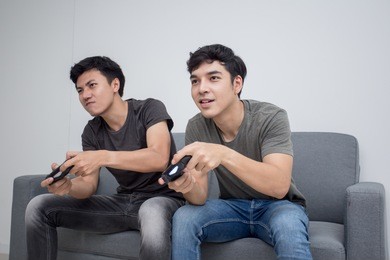 attractive asian man playing videogames on tv with friend. people play game with happy emotion togeyher. people lifestyle concept.