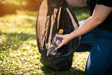 young volunteer picking up litte in to garbage bagsin in the park - ecology and volunteer concept