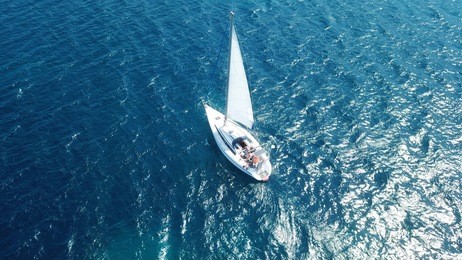 aerial photo of luxury yacht - sail boat cruising in deep blue waters of sanorini island, cyclades, aegean, greece