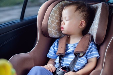 cute little asian 18 months / 1 year toddler baby boy child sleeping in modern car seat. child traveling safety on the road. safe way to travel fastened seat belts in vehicle with young kid concept