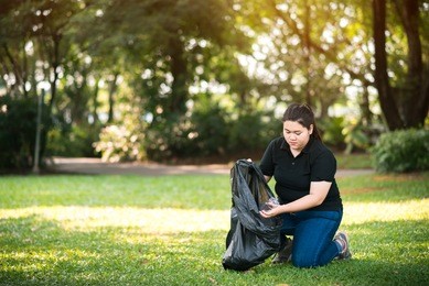young volunteer picking up litte in to garbage bagsin in the park - ecology and volunteer concept