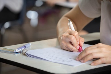 soft focus.hand high school or university student in uniform holding pencil writing on paper answer sheet.sitting on lecture chair taking final exam attending in examination room or classroom.