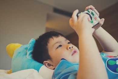 asian chinese boy playing smartphone on bed, watching smartphone, kid use phone and play game, child use mobile, addicted game and cartoon, boy play phone
