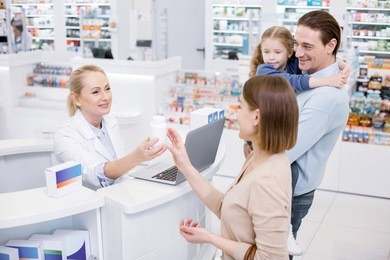 let me see. satisfied female pharmacist assisting family and posing in drugstore