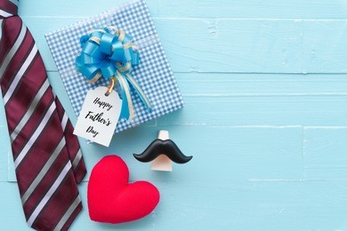happy fathers day concept. red tie, glasses, mustache, gift box with happy father's day text and handmade red heart on bright blue pastel wooden table background.
