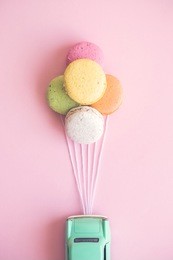 small retro car attached to colorful macaroons in form of helium balloons on pastel pink background minimal creative concept.