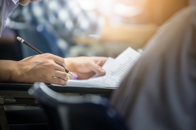 soft focus.hand high school or university student in uniform holding pencil writing on paper answer sheet.sitting on lecture chair taking final exam or study attending in examination room or classroom